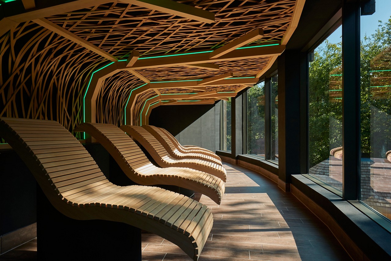 Wooden contoured lounging seats beneath a decorative wooden ceiling design.